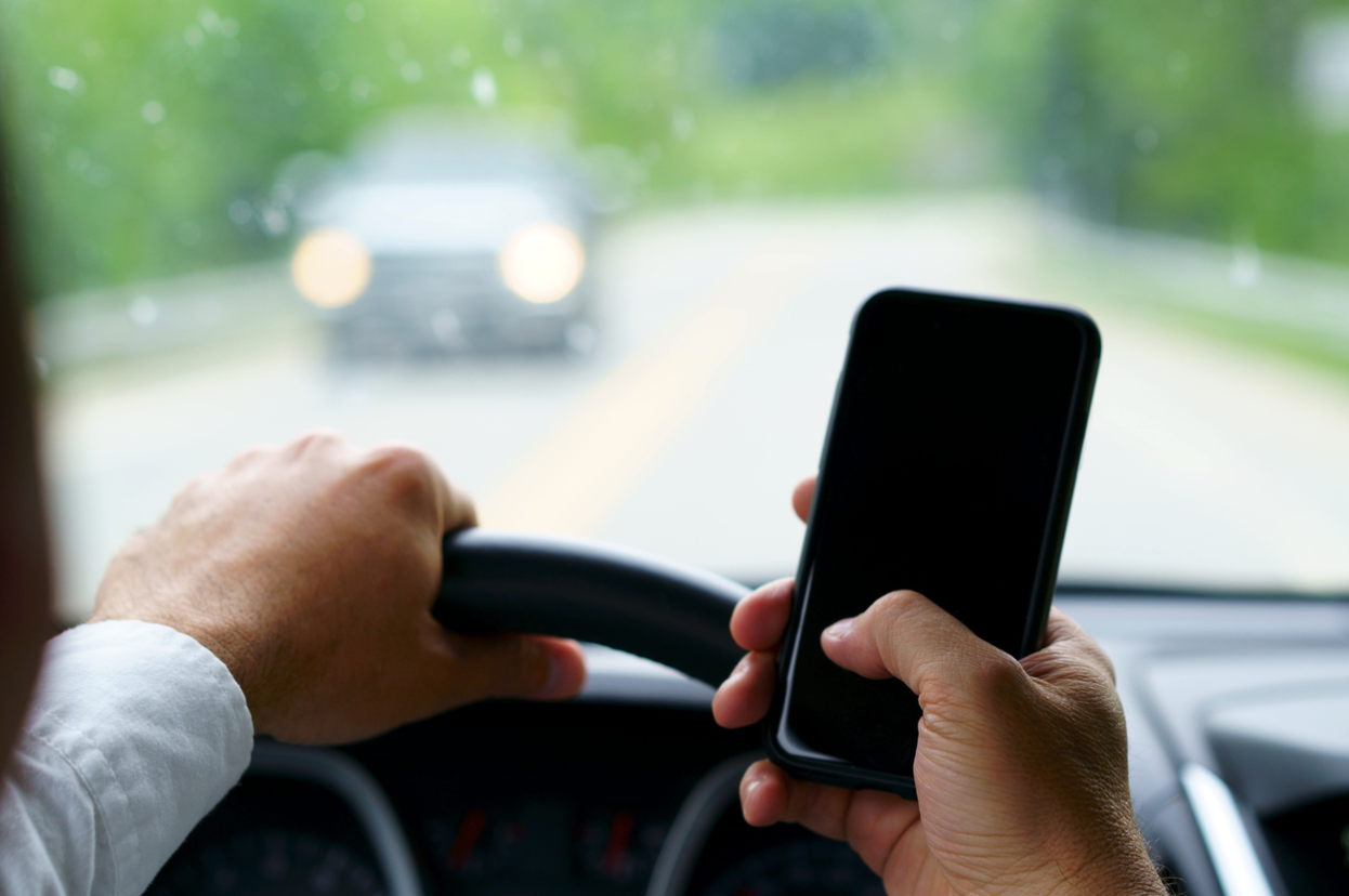 A man texting while driving, at risk of causing a car accident